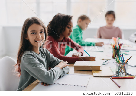 Happy Schoolgirl Sitting At Desk Smiling To Camera In Classroom 93311136