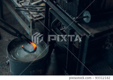 Blacksmith forges and tempering metal horseshoe in jar with water at forge. Blacksmith forges and tempering metal horseshoe in jar with water at forge. 93312182