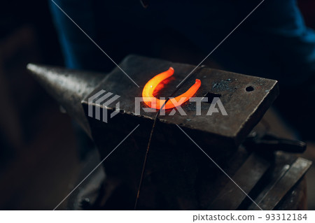 Blacksmith forges and making metal horseshoe with hammer and anvil at forge. Blacksmith forges and making metal horseshoe with hammer and anvil at forge. 93312184