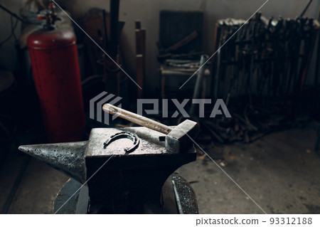 Blacksmith's hammer and horseshoe on metal anvil at forge. Overhead view 93312188