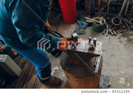 Blacksmith forges and makes metal horseshoe with hammer and anvil at forge. 93312193