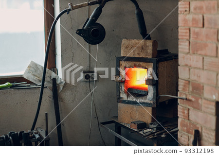 Blacksmith forge oven with hot flame. Smith heating iron piece of steel in fire of red-hot forge. Blacksmith forge oven with hot flame. Smith heating iron piece of steel in fire of red-hot forge. 93312198