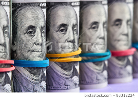 A row of rolled hundred dollar bills with rubber bands on purple background 93312224