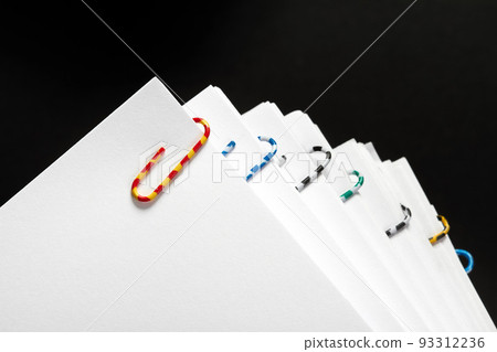 Stacks of papers with multicolored paper clips on a dark background Stacks of papers with multicolored paper clips on a dark background 93312236
