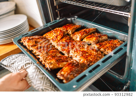 Woman cook taking out baked chicken from oven on baking sheet closeup Woman cook taking out baked chicken from oven on baking sheet closeup 93312982
