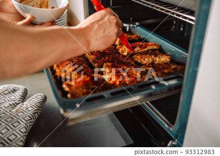 Woman cook taking out baked chicken from oven on baking sheet closeup Woman cook taking out baked chicken from oven on baking sheet closeup 93312983