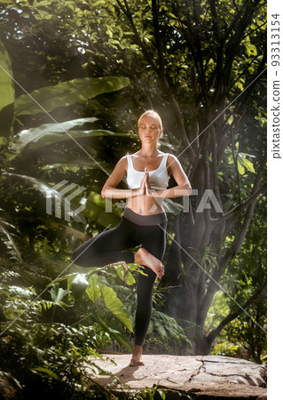 Portrait of young woman practicing yoga in tropic environment Portrait of young woman practicing yoga in tropic environment 93313154