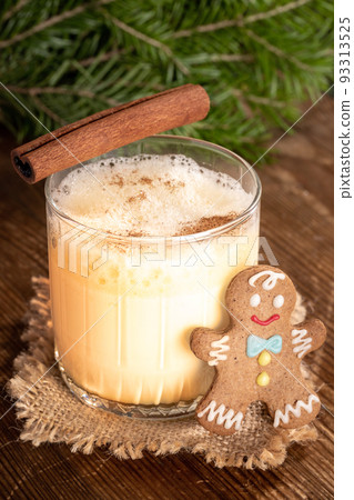 One glass with traditional homemade Christmas drink eggnog with cinnamon and small gingerbread man on rustic wooden table. Cozy Xmas time. Vertical orientation. Close up. Low key. Selective focus. One glass with traditional homemade Christmas drink eggnog with cinnamon and small gingerbread man on rustic wooden table. Cozy Xmas time. Vertical orientation. Close up. Low key. Selective focus. 93313525