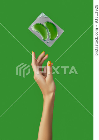 Womans hand with eye patches on green backgound. Face care beauty treatment steps concept 93313929