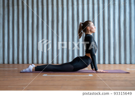 Woman in cobra pose, she exercising on floor her arms extended and upper body raised upward back hyperextended. 93315649