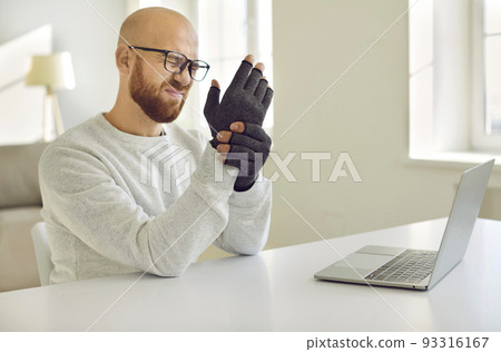 Man with rheumatoid arthritis kneads his hands on which he wears special compression gloves. Man with rheumatoid arthritis kneads his hands on which he wears special compression gloves. 93316167