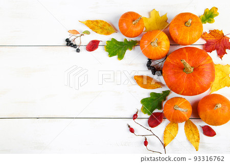 Autumn harvest. Ripe pumpkins, fallen leaves and berries on white wooden background. Thanksgiving and halloween concept. 93316762