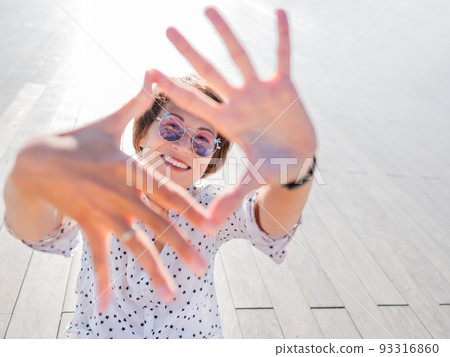 Smiling woman in colorful sunglasses has a rest on lawn in urban park. Nature in town. Relax outdoors after work. Summer vibes. Smiling woman in colorful sunglasses has a rest on lawn in urban park. Nature in town. Relax outdoors after work. Summer vibes. 93316860