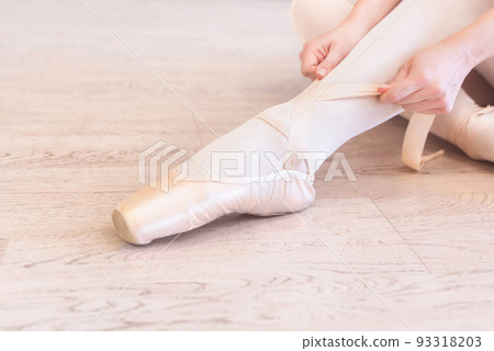 A seated ballerina tightens her pointe shoes A seated ballerina tightens her pointe shoes 93318203