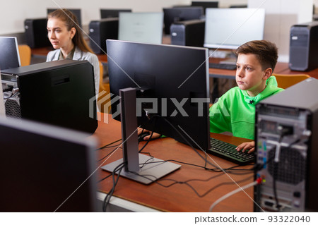Schoolboy using computer at lesson, teacher teaching pupils in class room 93322040