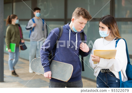 Two students in protective masks discuss past lessons at a college on street 93322079