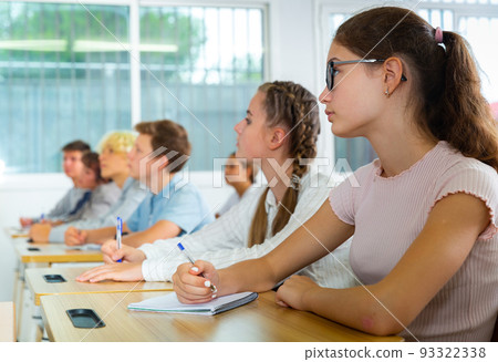 Teenagers listening to lecturer and writing in notebooks in classroom 93322338
