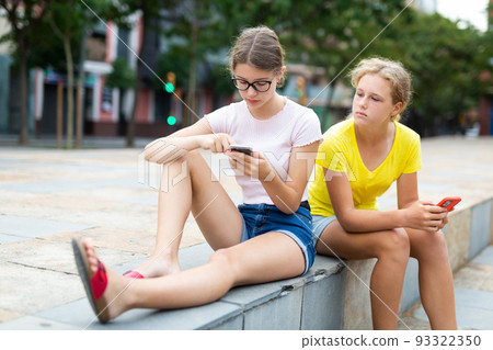 Two girlfriends with smartphones on street of summer city Two girlfriends with smartphones on street of summer city 93322350