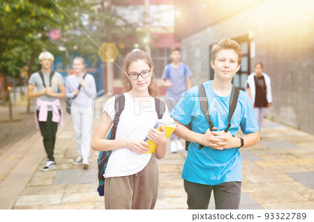 Teen schoolmates with backpacks and workbooks walking to college 93322789