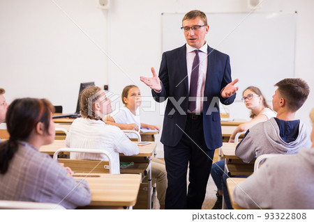 Friendly male teacher working with teen students in classroom 93322808
