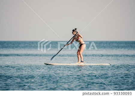Sea woman sup. Silhouette of happy middle aged woman in rainbow bikini, surfing on SUP board, confident paddling through water surface. Idyllic sunset. Active lifestyle at sea or river. Slow motion 93330093