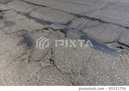 An old paved road with a lot of holes and damage 93331736