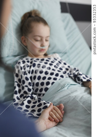 Hospitalized sick girl under treatment sleeping on patient bed while mother holding her hand. Ill little child resting inside hospital pediatric ward room while parent comforting her. Hospitalized sick girl under treatment sleeping on patient bed while mother holding her hand. Ill little child resting inside hospital pediatric ward room while parent comforting her. 93332353