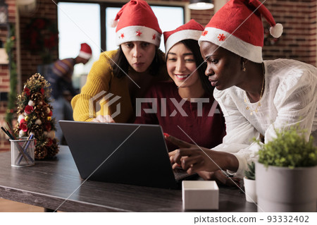 Diverse team of women working on startup business in festive office with christmas tree and decorations. Doing teamwork and celebrating xmas time with seasonal holiday ornaments. Diverse team of women working on startup business in festive office with christmas tree and decorations. Doing teamwork and celebrating xmas time with seasonal holiday ornaments. 93332402