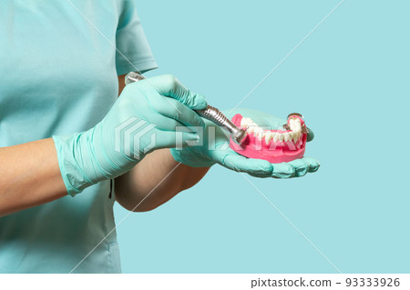 Head of high-speed dental handpiece with bur and a layout of the human jaw in dentist's hands. 93333926