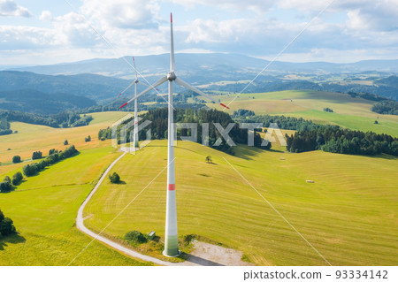 Aerial view of wind turbines propeller in the yellow field with amazing view on the mountains in sunny day. Environment friendly and renewable energy resource.  93334142