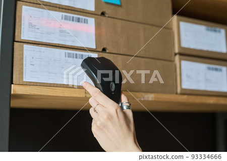 Close-up of woman scanning barcodes on parcels with scanner while working in warehouse 93334666