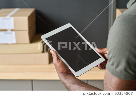 Close-up of warehouse worker checking track numbers of parcels on digital tablet during his work in warehouse 93334807