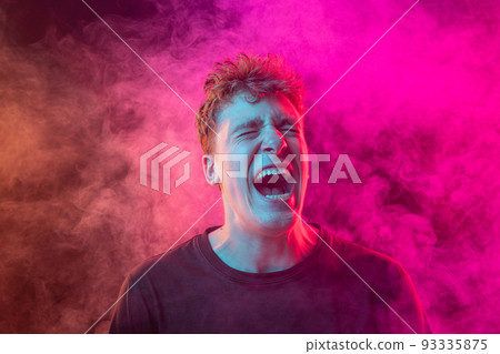 Shouting excited young man with bright emotions isolated over pink background with smoke. Concept of mental health, art, human emotions Shouting excited young man with bright emotions isolated over pink background with smoke. Concept of mental health, art, human emotions 93335875