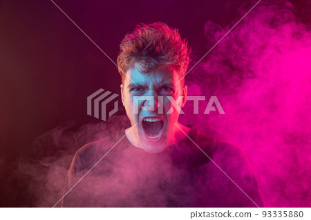 Shouting excited young man with bright emotions isolated over pink background with smoke. Concept of mental health, art, human emotions Shouting excited young man with bright emotions isolated over pink background with smoke. Concept of mental health, art, human emotions 93335880