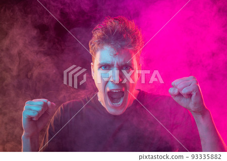 Shouting angry young man with bright emotions isolated over pink background with smoke. Concept of mental health, art, human emotions Shouting angry young man with bright emotions isolated over pink background with smoke. Concept of mental health, art, human emotions 93335882