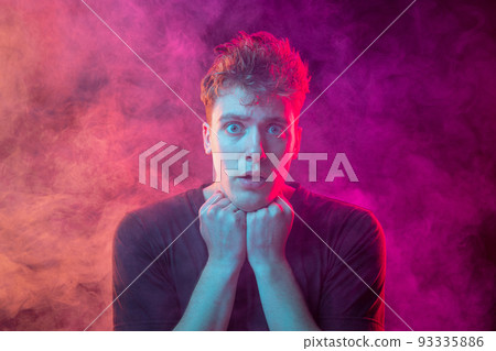 Smoke enveloped young man. Model looking at camera isolated over magenta background with clouds of smoke. Concept of mental health, art, emotions 93335886