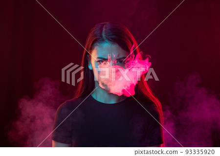 Angry young girl with dark hair releases smoke from the mouth isolated over pink background. Concept of mental health, art, human emotions Angry young girl with dark hair releases smoke from the mouth isolated over pink background. Concept of mental health, art, human emotions 93335920
