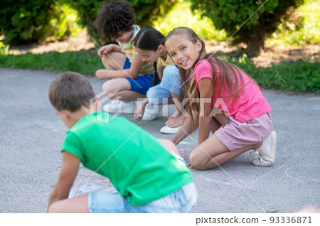 Blonde girl with friends drawing with crayons in park Blonde girl with friends drawing with crayons in park 93336871