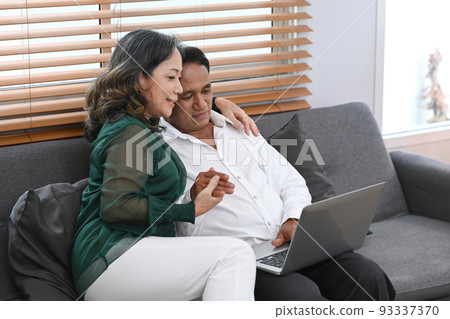 Senior couple watching video or shopping online on laptop together, resting on couch and spending time together Senior couple watching video or shopping online on laptop together, resting on couch and spending time together 93337370
