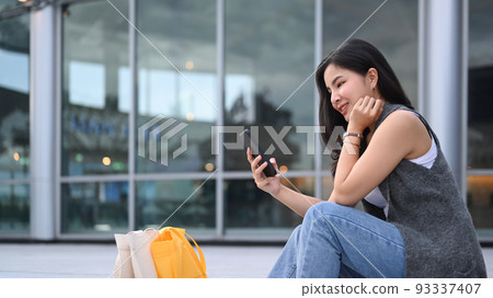Stylish young asian woman sitting on the stairs outdoors and using smart phone Stylish young asian woman sitting on the stairs outdoors and using smart phone 93337407