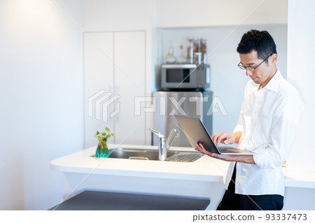 A man operating a computer while standing in the dining room A man operating a computer while standing in the dining room 93337473