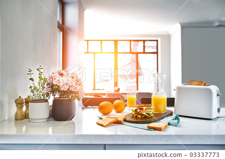 White electric bread toaster with orange juice with sandwich on kitchen table. Breakfast in the cozy kitchen. Sun flare White electric bread toaster with orange juice with sandwich on kitchen table. Breakfast in the cozy kitchen. Sun flare 93337773