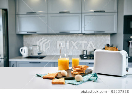 Toaster with fresh toast, eggs and glass of orange juice on a light kitchen table 93337828