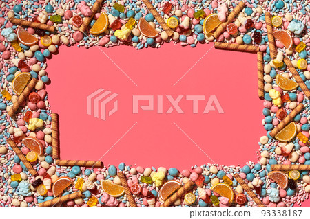 Multicolored glazed dragees and other sweets are arranged in the form of a frame on a coral background. Multicolored glazed dragees and other sweets are arranged in the form of a frame on a coral background. 93338187