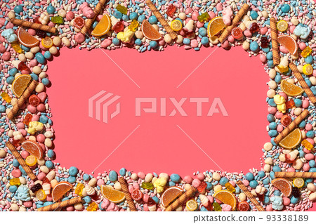 Multicolored glazed dragees and other sweets are arranged in the form of a frame on a coral background. Multicolored glazed dragees and other sweets are arranged in the form of a frame on a coral background. 93338189
