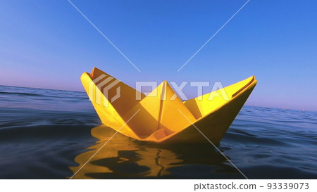 Yellow paper boat floats on surface of blue water waves of sea close-up. Clear blue sky on sunny summer day. Concept adventures travelling vacation holiday rest tourism voyager dream. Slow motion 93339073