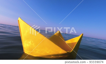 Yellow paper boat floats on surface of blue water waves of sea close-up. Clear blue sky on sunny summer day. Concept adventures travelling vacation holiday rest tourism voyager dream. Slow motion 93339074