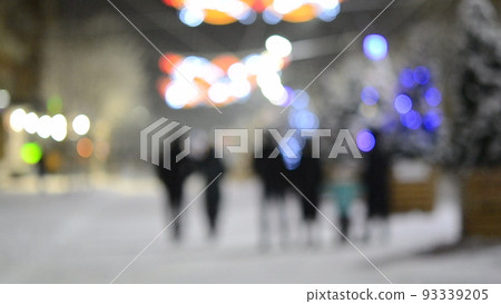 Blurred background. City street during snowfall at winter night. Beautiful illumination and decoration on street. New Year Christmas holidays celebration. Lanterns garlands on trees. Blurred background. City street during snowfall at winter night. Beautiful illumination and decoration on street. New Year Christmas holidays celebration. Lanterns garlands on trees. 93339205