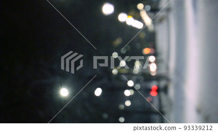 Blurred background. City view, lights, falling snow, night, street, bokeh spots of headlights of moving cars. Diffuse Urban backdrop winter scenery of street in city at night. Vertical video 93339212