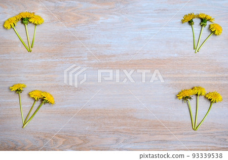 Place for text on a wooden textured surface and bouquets of yellow dandelions in the corners for a positive mood. 93339538